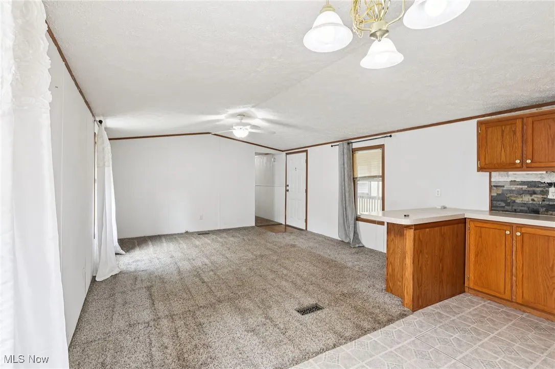 Kitchen featuring brown cabinets, a peninsula, light carpet, light countertops, and backsplash