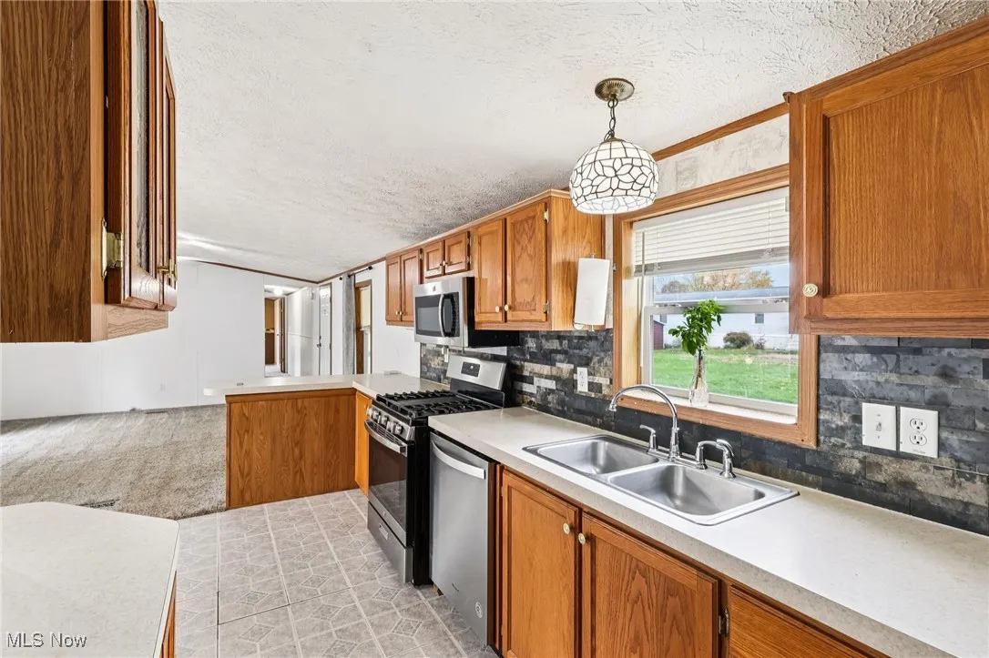 Kitchen featuring a textured ceiling, brown cabinets, stainless steel appliances, backsplash, and decorative light fixtures