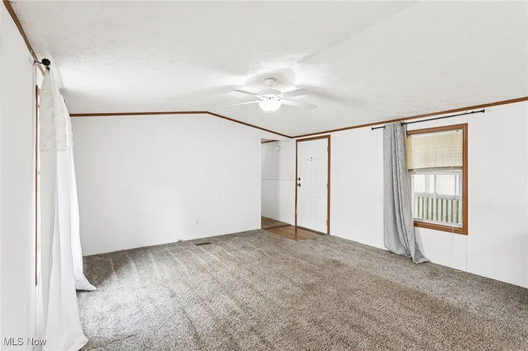 Unfurnished bedroom with carpet flooring, ornamental molding, a textured ceiling, lofted ceiling, and a ceiling fan