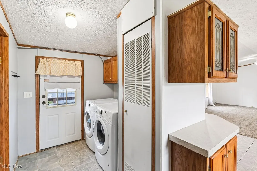Laundry room with a textured ceiling, a heating unit, cabinet space, washing machine and clothes dryer, and light tile patterned floors