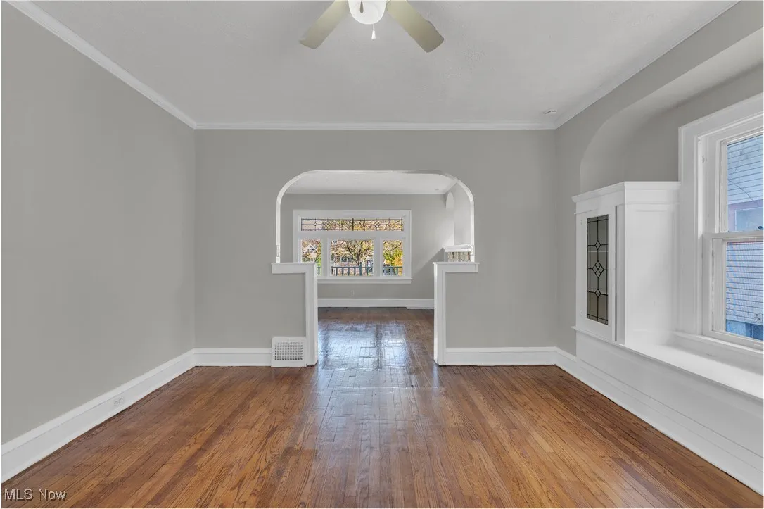 Empty room featuring dark wood-style floors, ornamental molding, and a ceiling fan