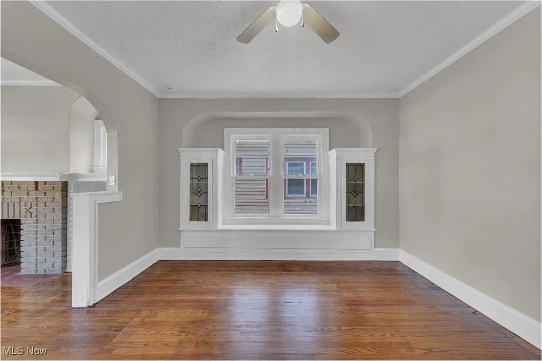 Spare room with ornamental molding, wood-type flooring, a fireplace, a textured ceiling, and arched walkways