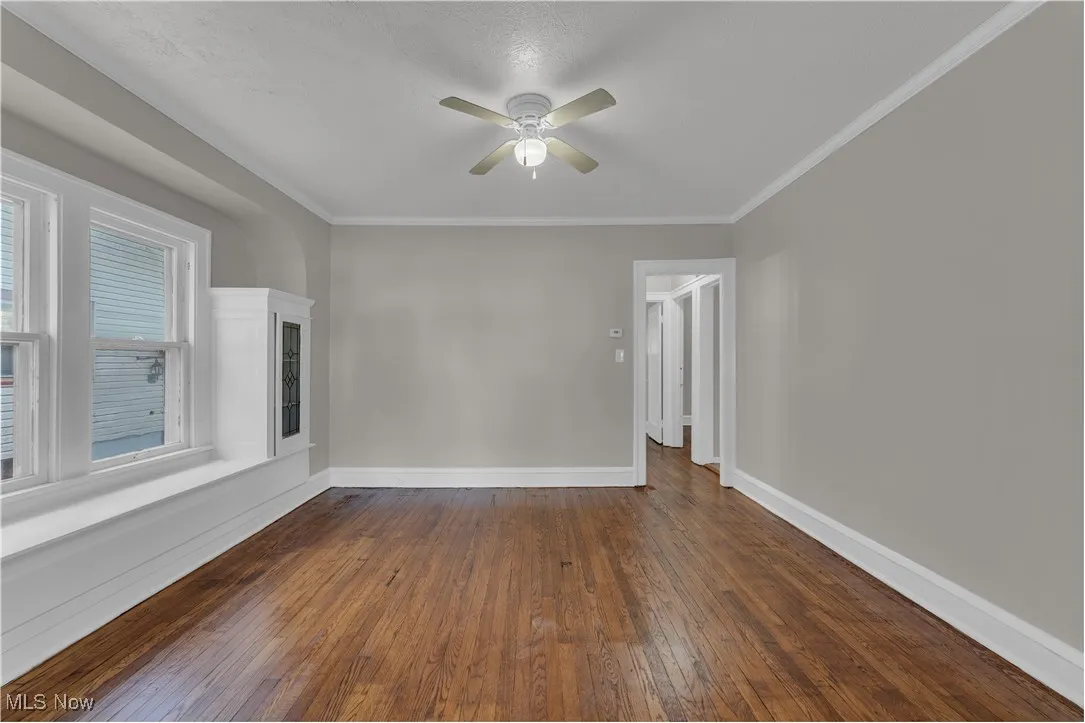 Unfurnished room featuring dark wood-type flooring, ornamental molding, and ceiling fan