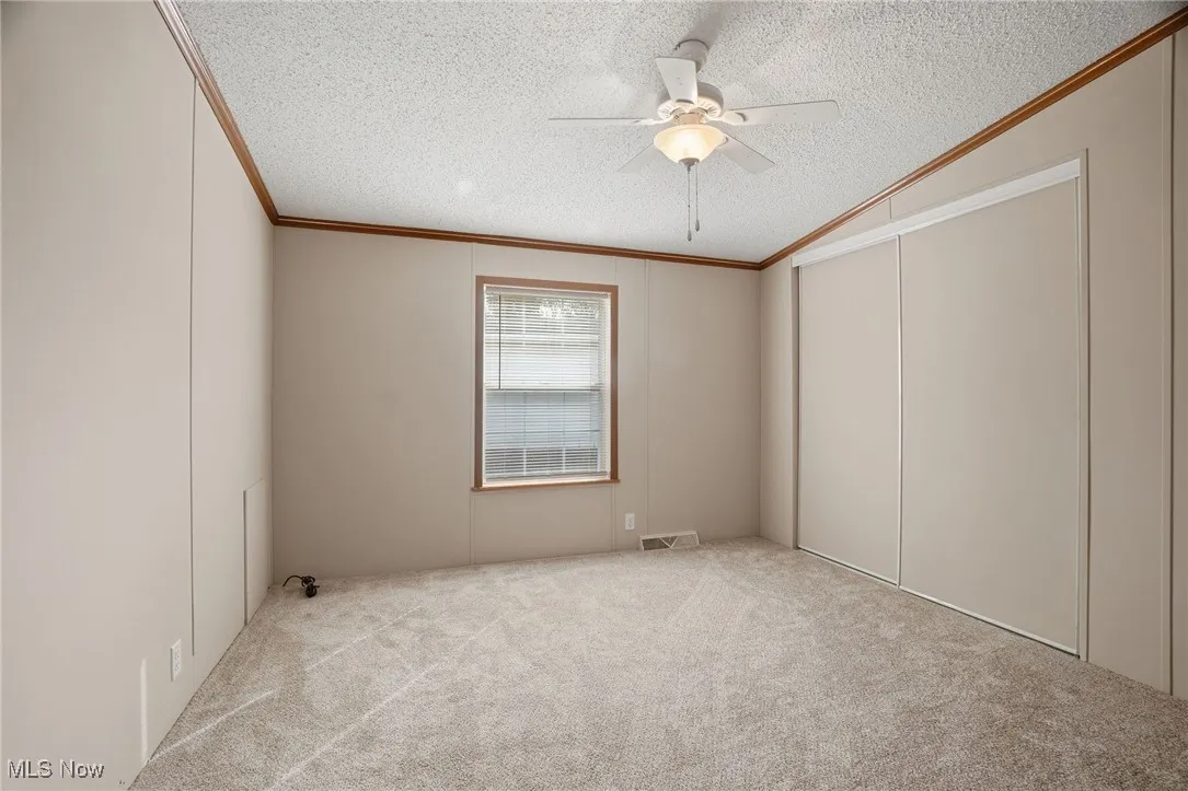 Unfurnished bedroom featuring ornamental molding, a textured ceiling, ceiling fan, and carpet floors