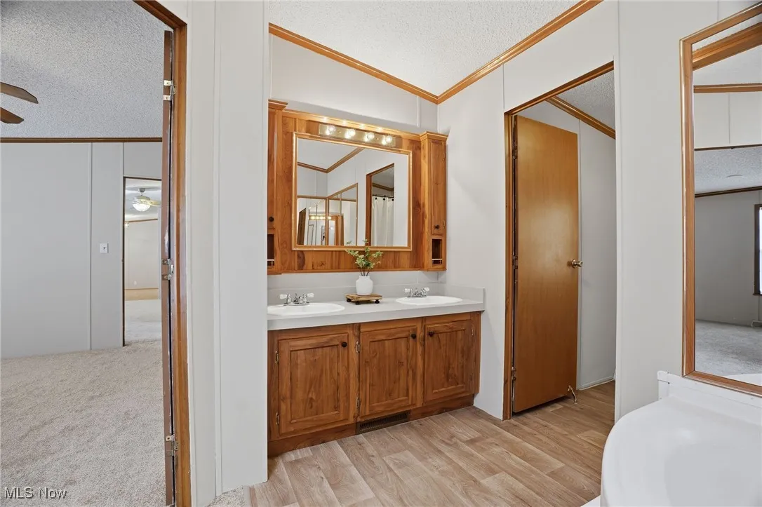 Bathroom with a textured ceiling, crown molding, double vanity, vaulted ceiling, and light wood finished floors