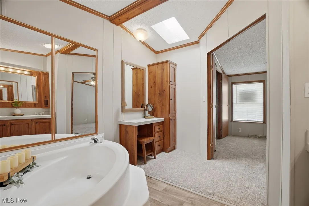 Bathroom featuring a textured ceiling, crown molding, vaulted ceiling, a skylight, and a bathtub