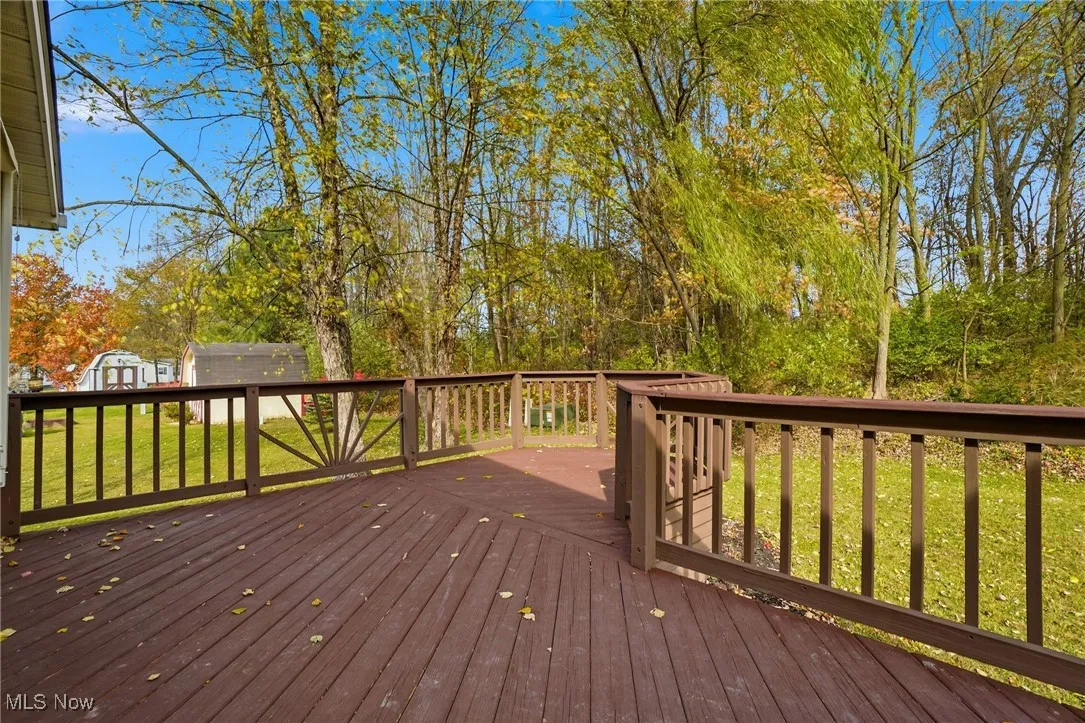 Wooden terrace with a yard, a storage unit, and view of wooded area
