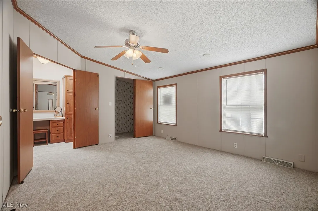 Unfurnished bedroom with crown molding, a textured ceiling, light carpet, ceiling fan, and vaulted ceiling