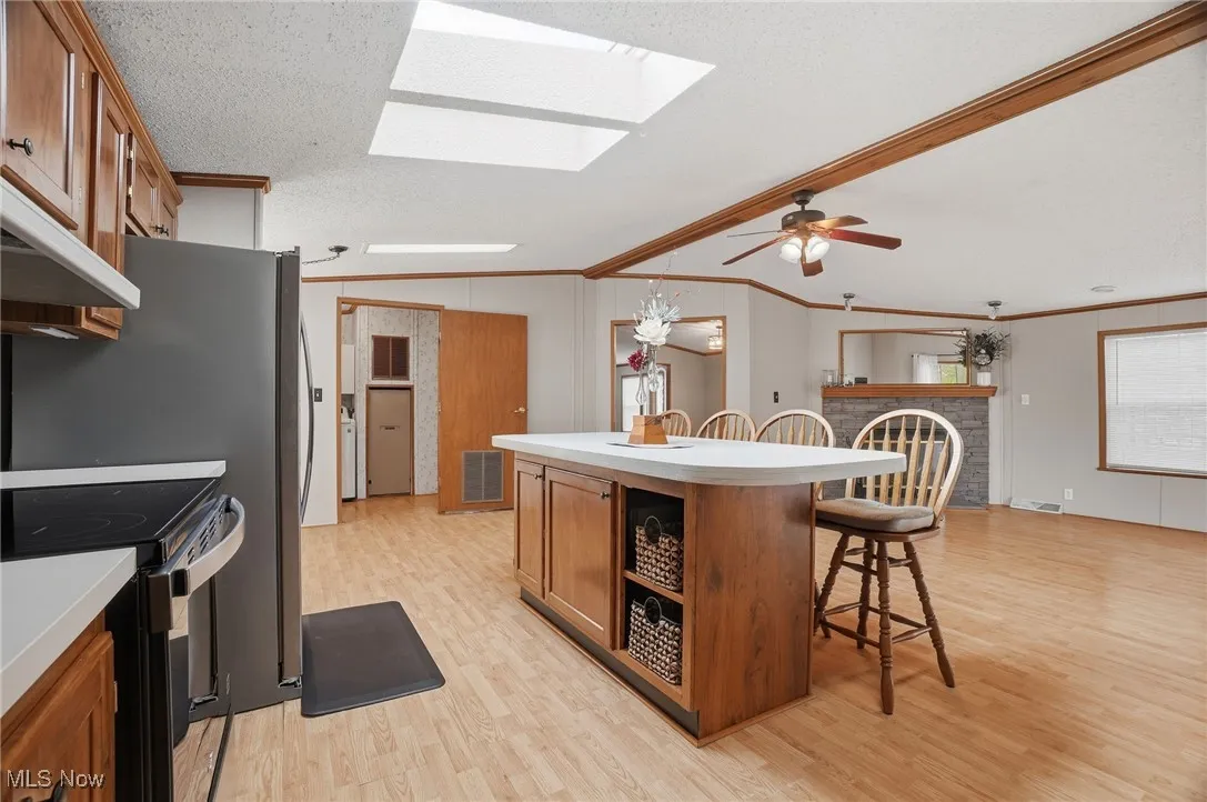 Kitchen with brown cabinets, a breakfast bar area, vaulted ceiling, open shelves, and light wood finished floors