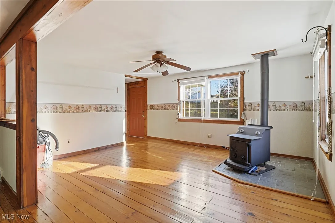 Unfurnished living room featuring a wood stove, wood-type flooring, and a ceiling fan