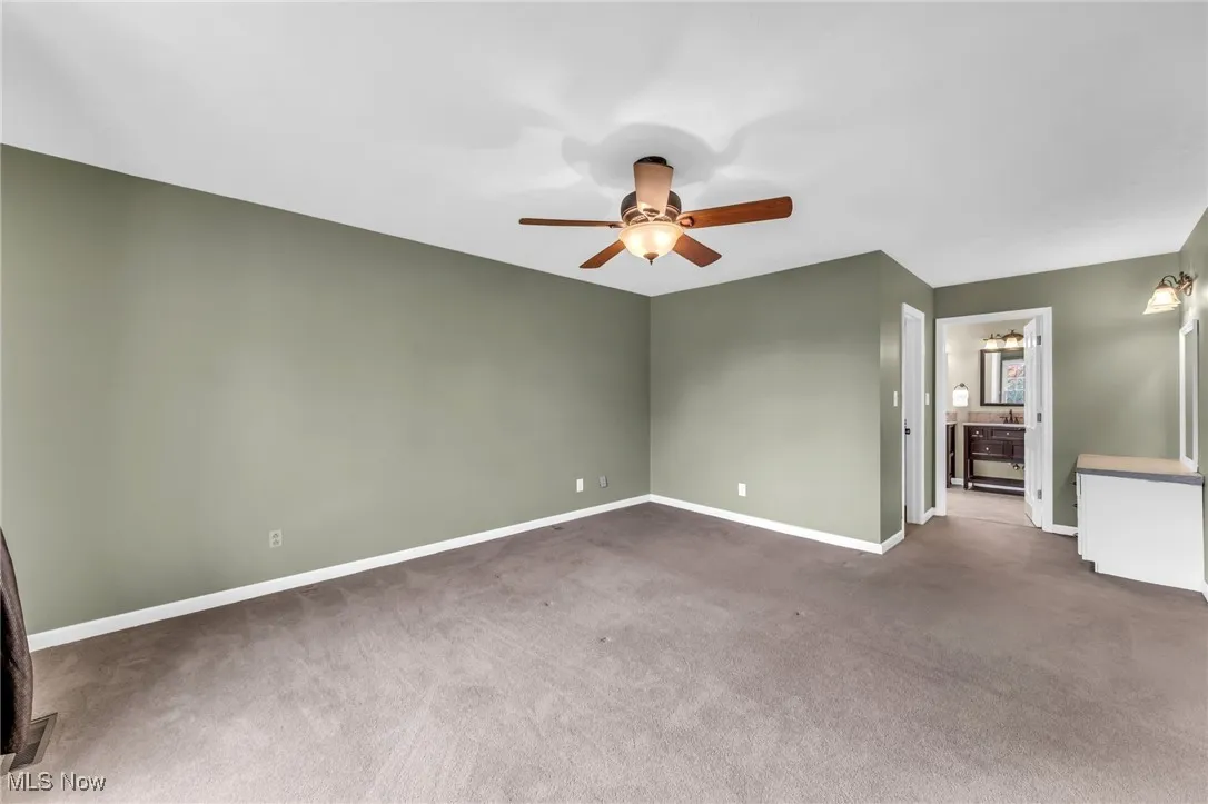 View of Primary Bedroom with dimmable ceiling fan fixture. Ensuite Bath can be seen through doorway at center. Dressing area can be seen at right.