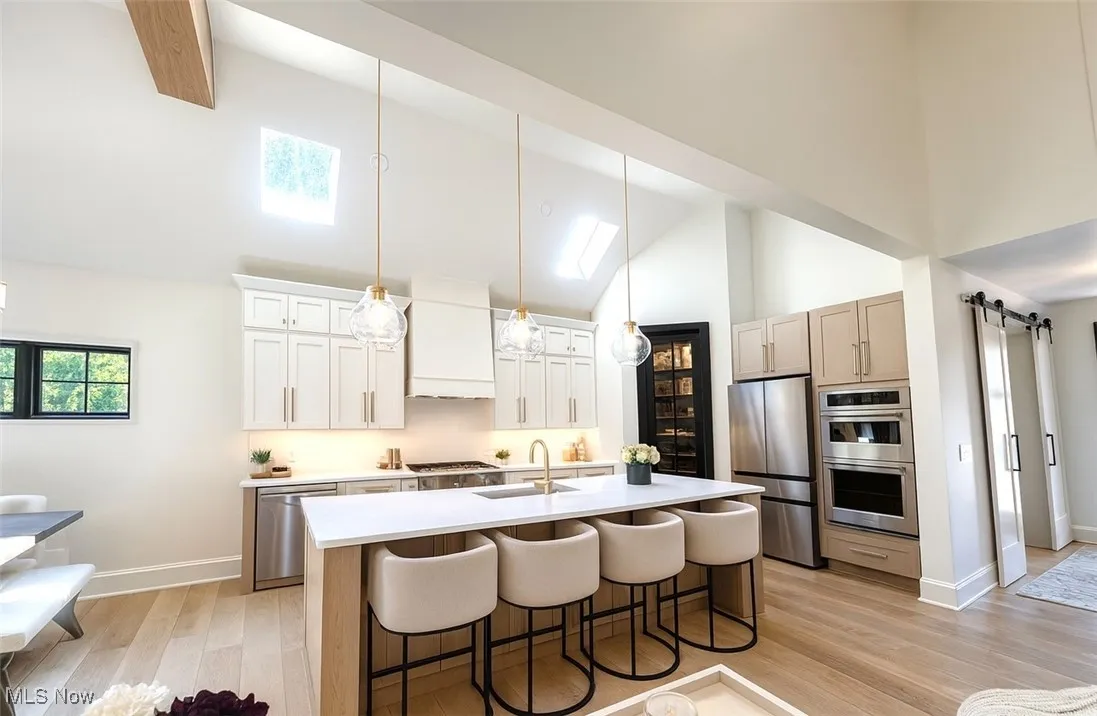 Kitchen featuring a barn door, hanging light fixtures, a skylight, a kitchen breakfast bar, and high vaulted ceiling