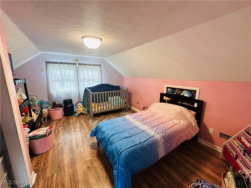 Bedroom with lofted ceiling, wood finished floors, and a textured ceiling