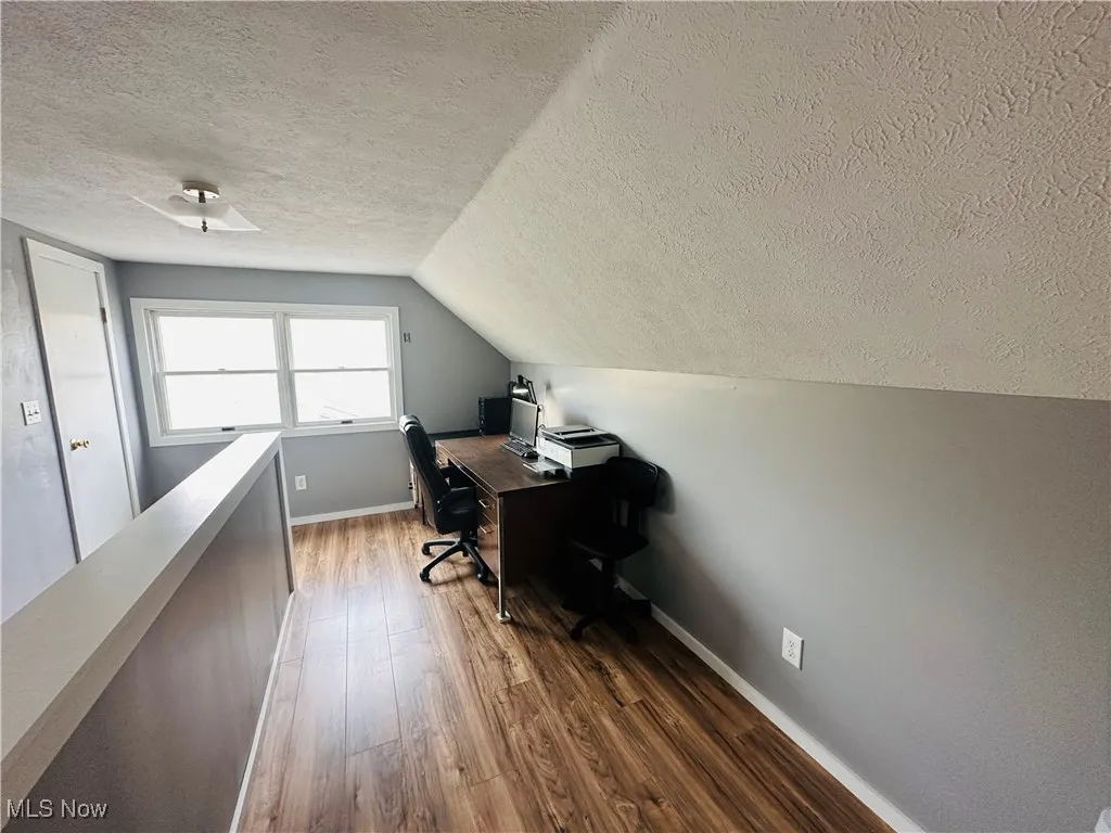 Office with a textured ceiling, dark wood-style floors, and vaulted ceiling