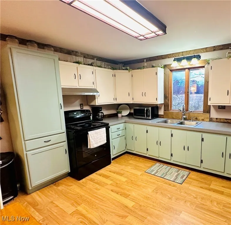 Kitchen with green cabinets, electric range, stainless steel microwave, light wood finished floors, and white cabinets