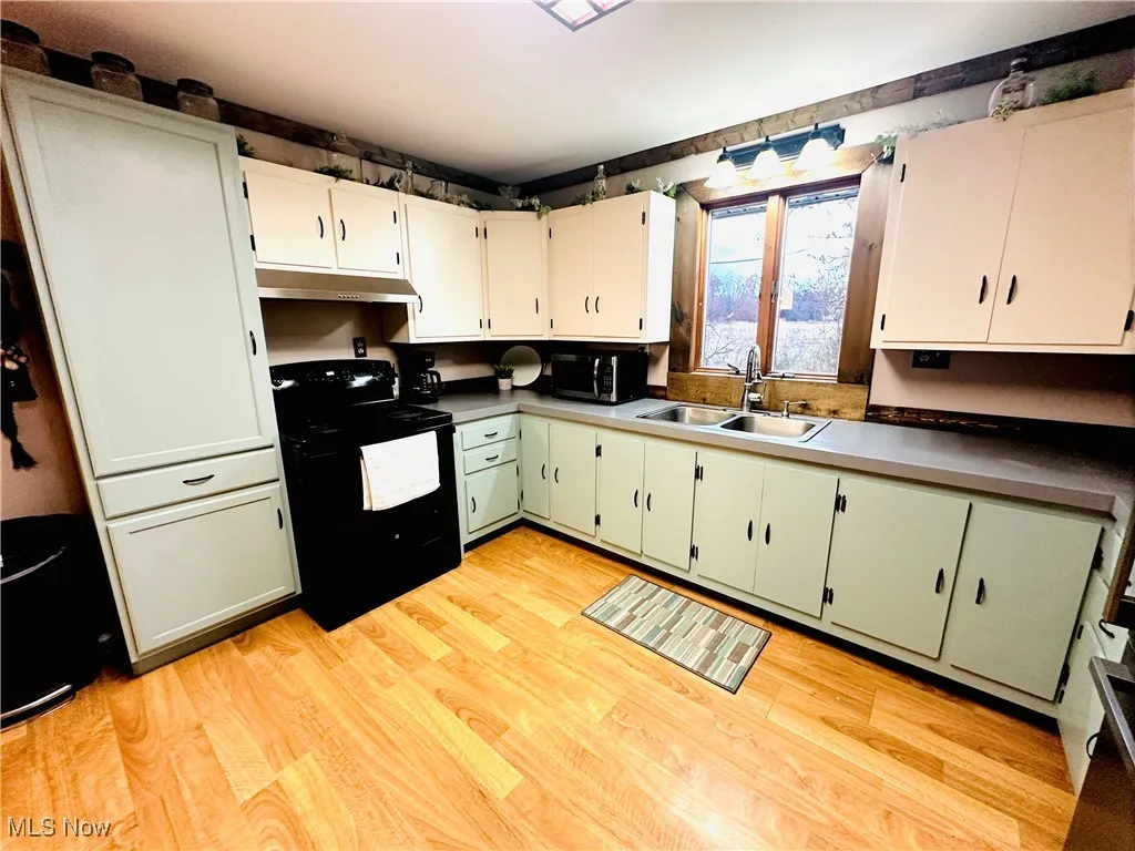 Kitchen featuring green cabinets, black electric range oven, light wood finished floors, and white cabinetry