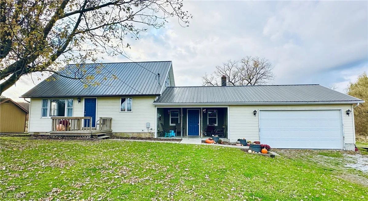 View of front facade with driveway, a front lawn, a metal roof, a garage, and a patio area