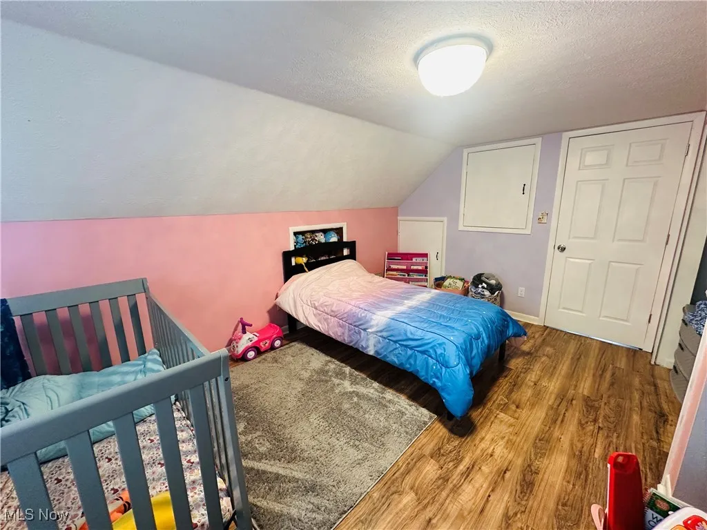 Bedroom with a textured ceiling, wood finished floors, and lofted ceiling