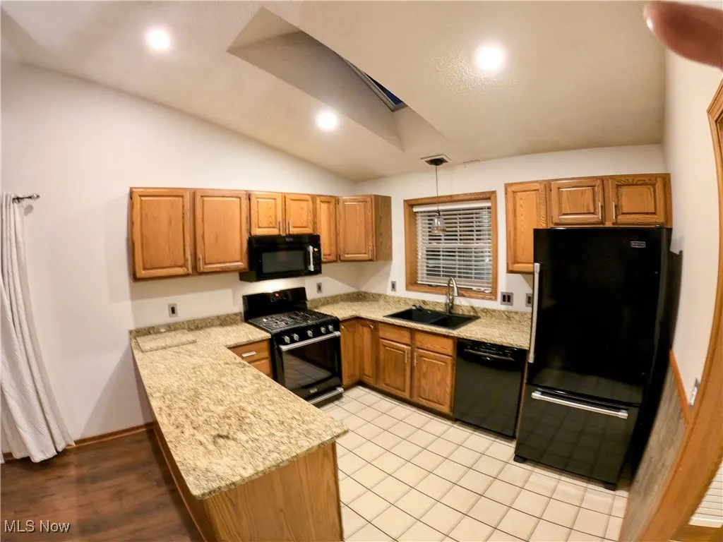 Kitchen with black appliances, a peninsula, lofted ceiling, brown cabinets, and recessed lighting
