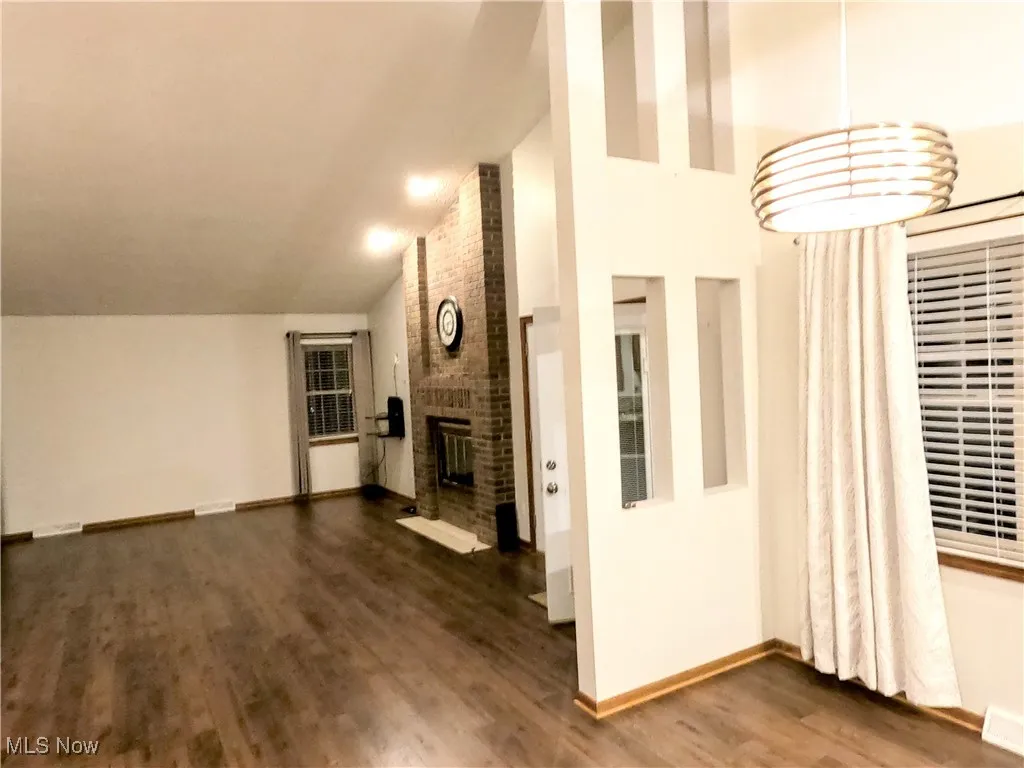 Unfurnished living room featuring vaulted ceiling, a fireplace, and dark wood-type flooring