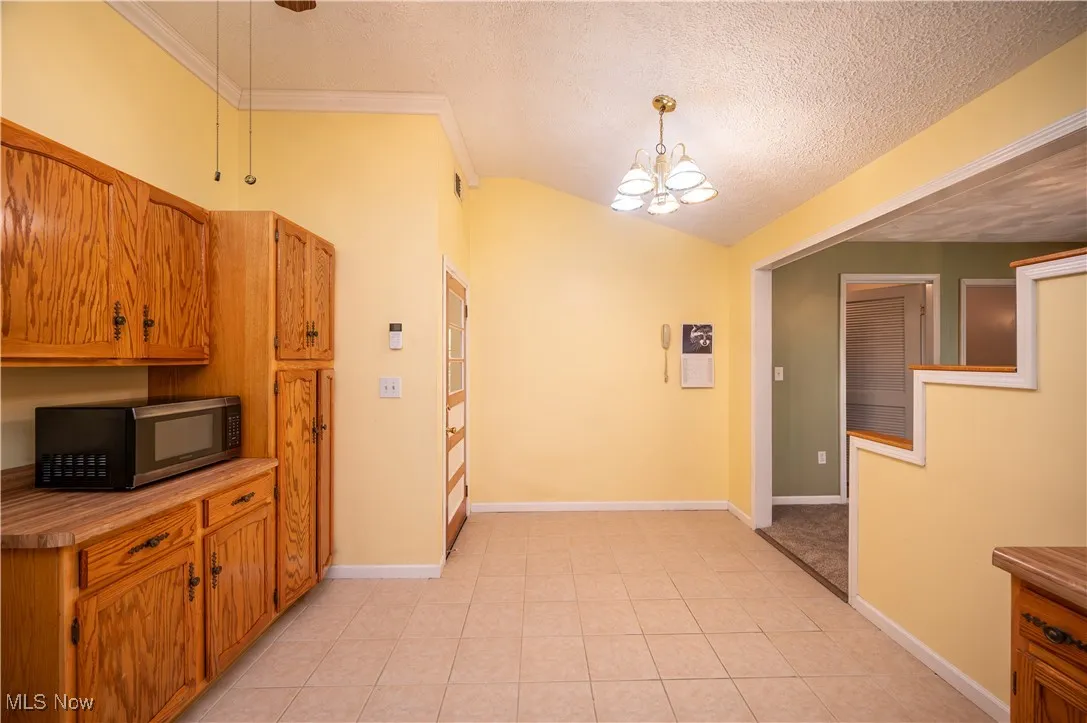 Eat-in kitchen area featuring wooden cabinetry, stainless steel microwave, ceramic tile flooring, vaulted ceiling, and hanging light fixture w/ fan