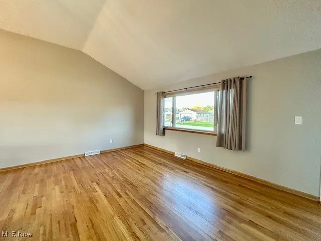 Unfurnished room featuring light wood finished floors and lofted ceiling