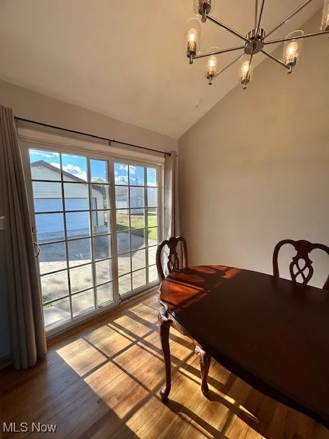Dining area with vaulted ceiling, wood finished floors, a chandelier, and a water view