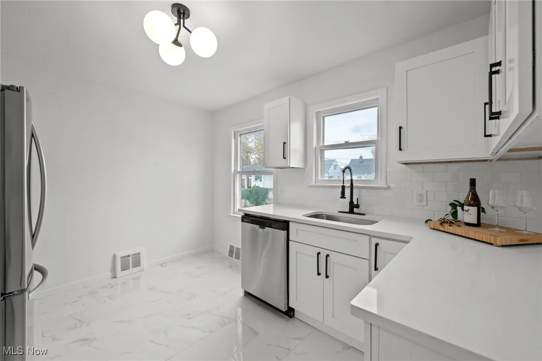 Kitchen featuring stainless steel appliances, white cabinets, backsplash, light marble finish flooring, and light stone countertops