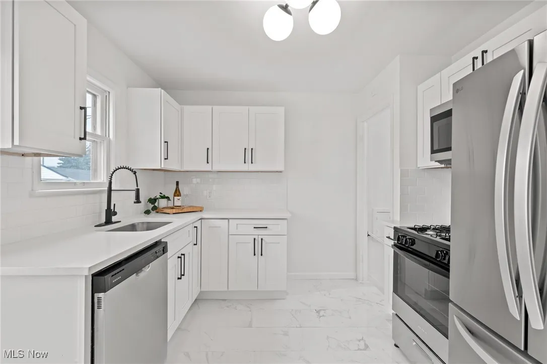 Kitchen with stainless steel appliances, tasteful backsplash, white cabinetry, and light marble finish flooring