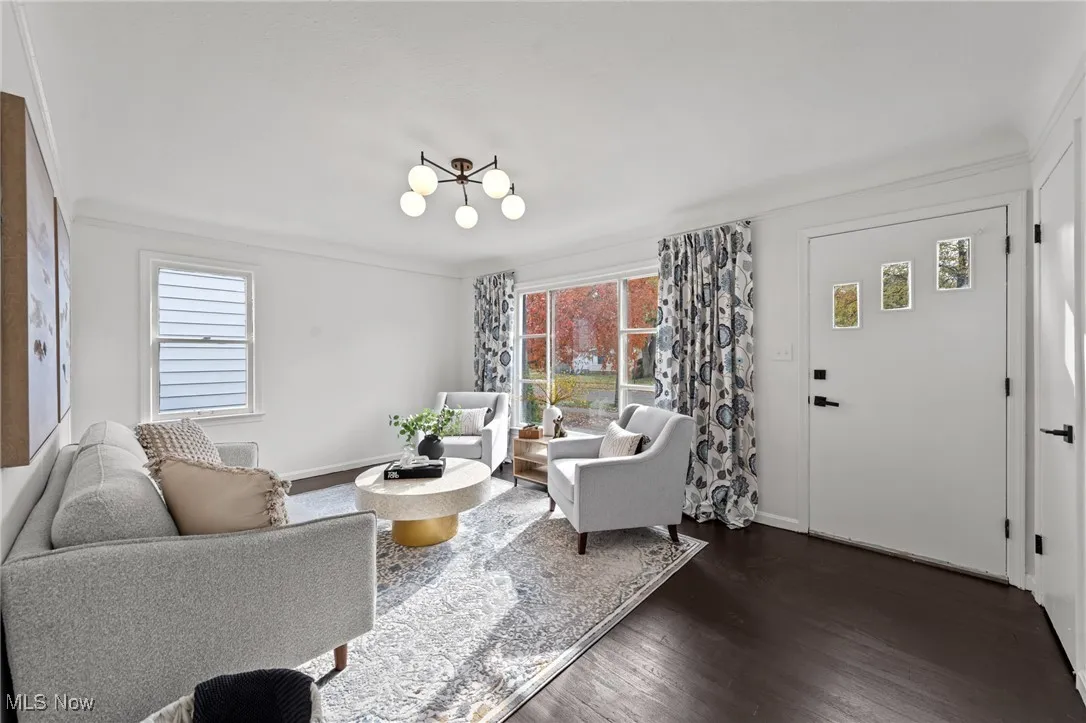 Living area with dark wood finished floors, ornamental molding, and a chandelier