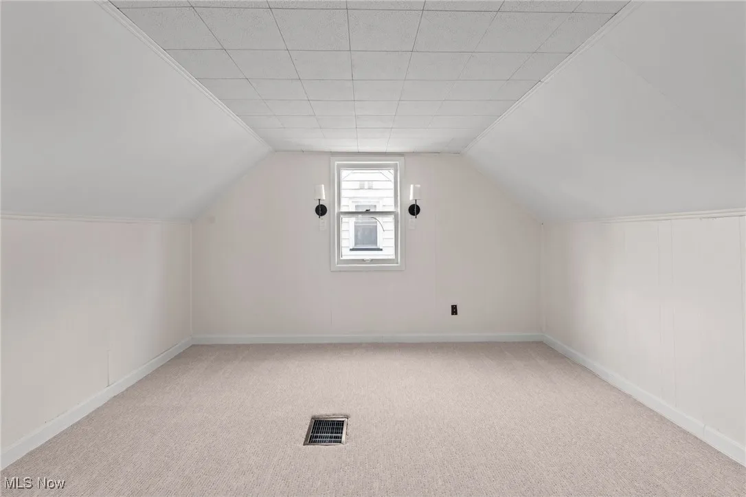 Additional living space with light colored carpet and vaulted ceiling