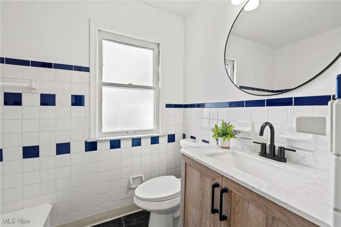 Full bath featuring tile walls, vanity, a tub to relax in, and wainscoting