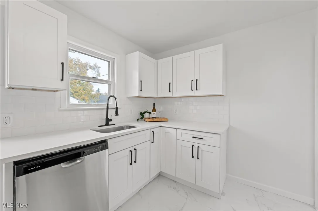 Kitchen featuring stainless steel dishwasher, light marble finish floors, white cabinets, backsplash, and light stone counters