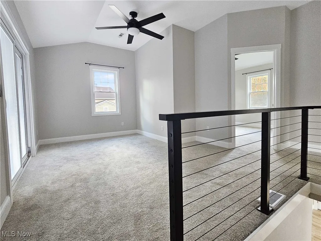 Empty room featuring light colored carpet, vaulted ceiling, and ceiling fan