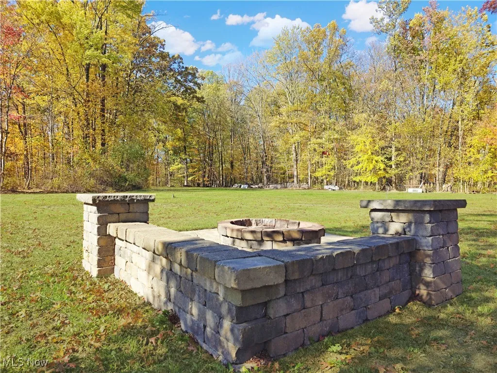View of grassy yard featuring a fire pit and a forest view