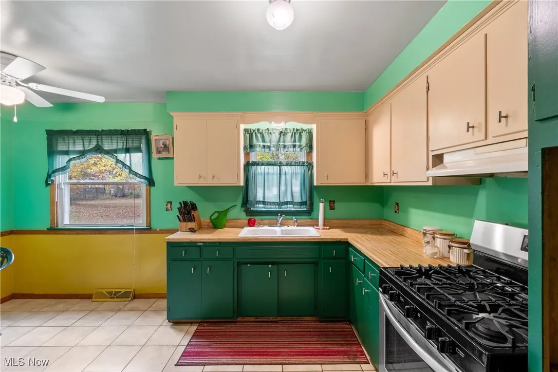 Kitchen featuring gas stove, light countertops, under cabinet range hood, and light tile patterned floors