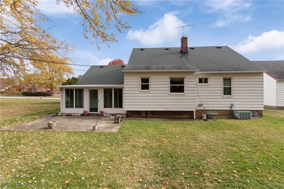 Rear view of property with a sunroom, a yard, a chimney, a patio area, and roof with shingles
