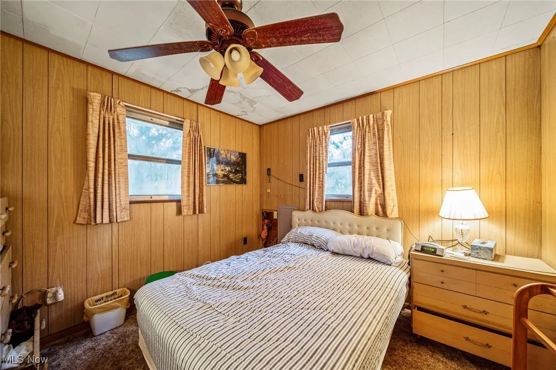 Bedroom 2 with windows facing front & side yards, wood panel walls and ceiling fan