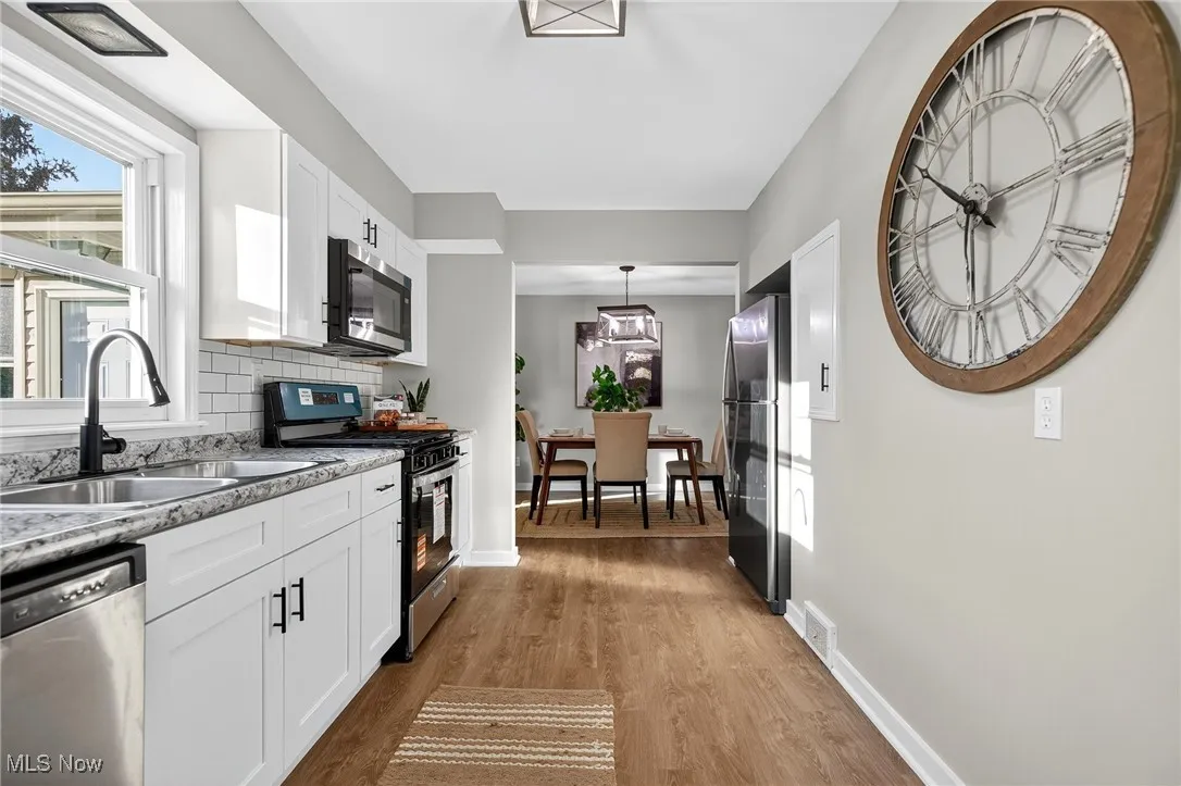 Kitchen featuring appliances with stainless steel finishes, white cabinets, light wood-type flooring, hanging light fixtures, and tasteful backsplash