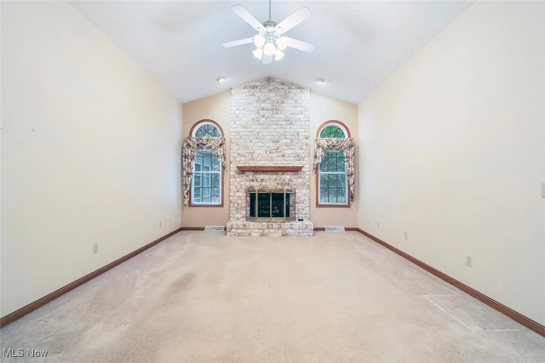 Unfurnished living room featuring vaulted ceiling, light carpet, a fireplace, and a ceiling fan