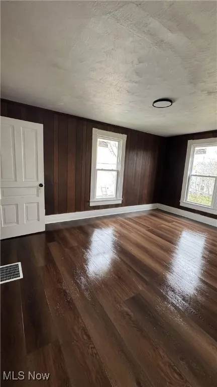 Empty room with a textured ceiling, dark wood-style flooring, and wooden walls