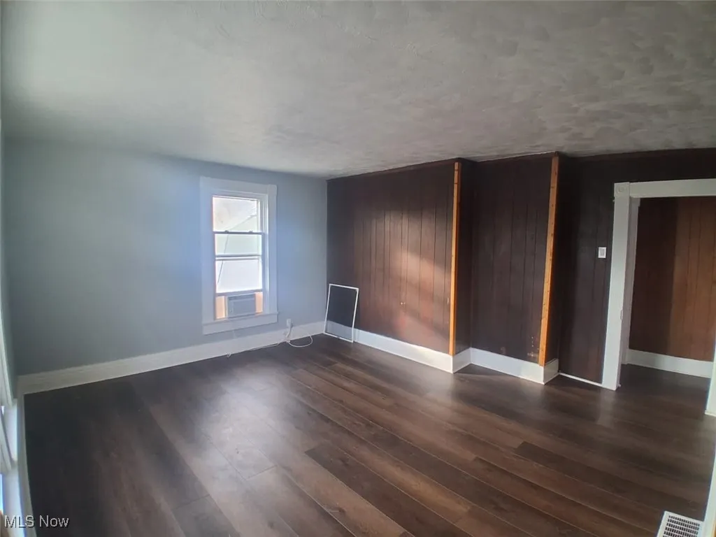 Empty room featuring dark wood-type flooring, a textured ceiling, and wooden walls