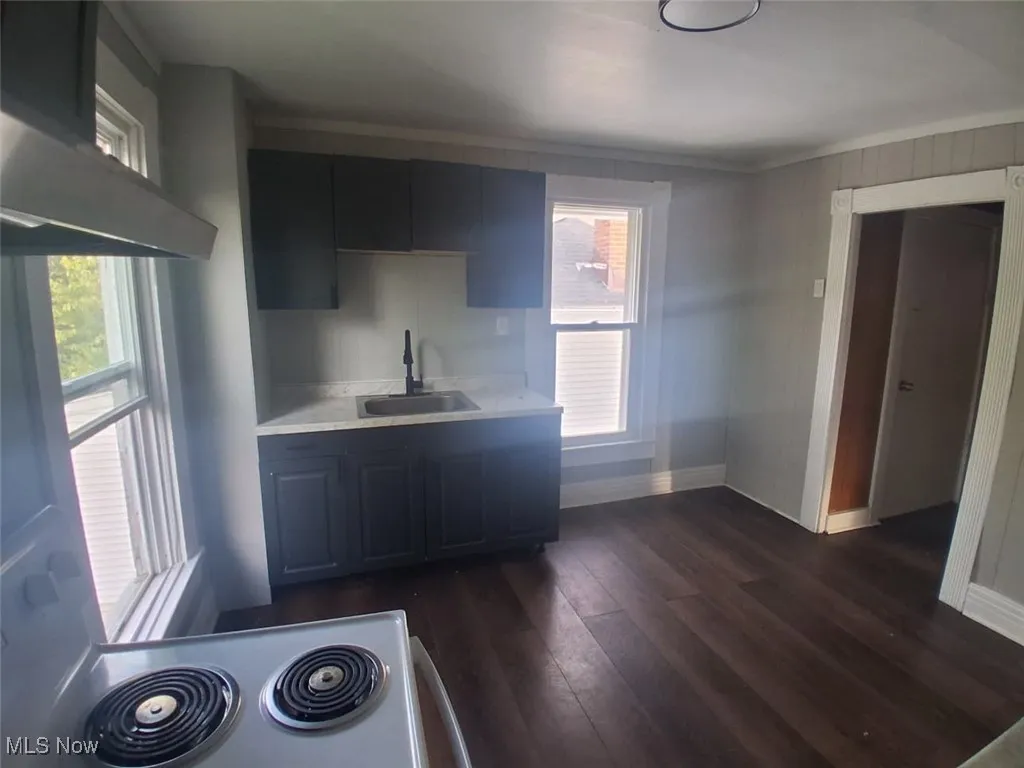 Kitchen featuring wall chimney range hood, dark wood-style flooring, and light stone countertops