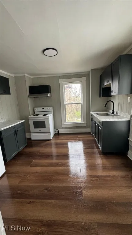 Kitchen with light countertops, dark wood-style flooring, white electric range oven, wooden walls, and ventilation hood