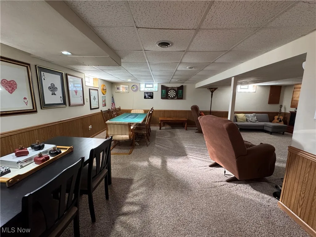 Recreation room featuring a paneled ceiling, carpet floors, healthy amount of natural light, and a wainscoted wall