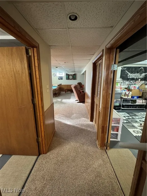 Corridor with a paneled ceiling, carpet flooring, wainscoting, and wood walls