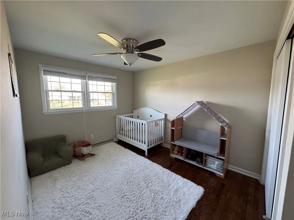 Bedroom featuring dark wood-style flooring, a nursery area, and a ceiling fan