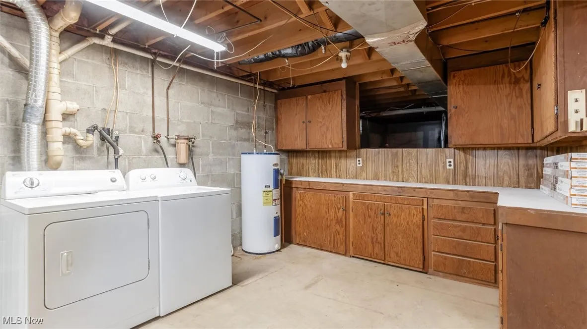 Laundry area featuring unfinished concrete flooring, electric water heater, independent washer and dryer, and cabinet space