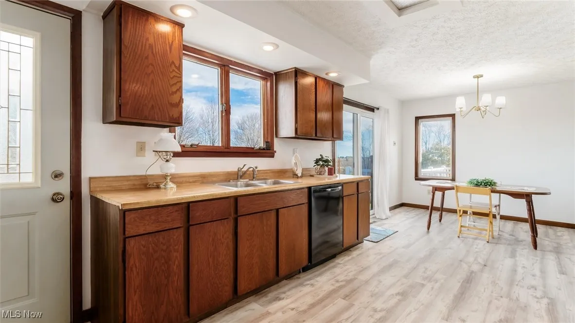 Kitchen featuring light countertops, light wood finished floors, decorative light fixtures, black dishwasher, and a textured ceiling