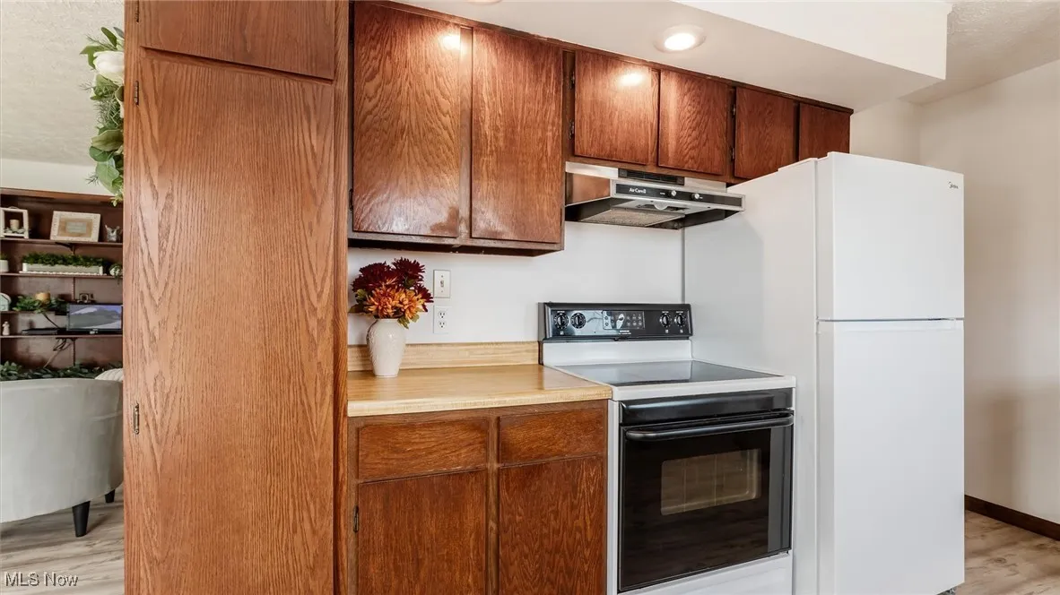 Kitchen with light wood-type flooring, black range with electric cooktop, light countertops, under cabinet range hood, and brown cabinets